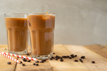 Iced coffee in transparent glasses with ice and straws, on a wooden background, a cooling drink