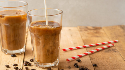 Cold coffee pouring in cream, milk in transparent glasses with ice and straws, on a wooden background, a cooling drink, refreshing