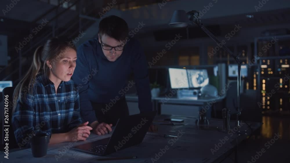 Poster Industrial Engineering Facility: Female Engineer Working on Desktop Computer, Project Manager Stands Beside and Explains Specifics of the Task and Project Details. Working Late on Engine Prototype
