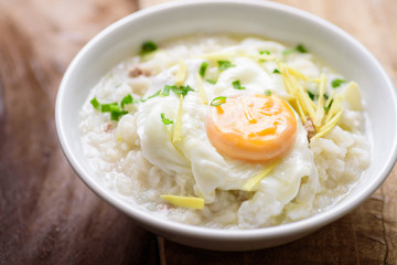 Thai rice soup or soft-boiled rice with pork and egg in the bowl on wooden background