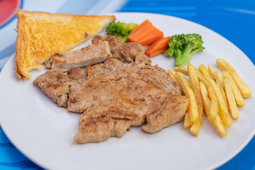 Kurobuta pork chop with vegetable and french fries in white dish.