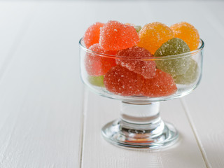 Glass bowl filled with colorful marmalade on a white wooden table.