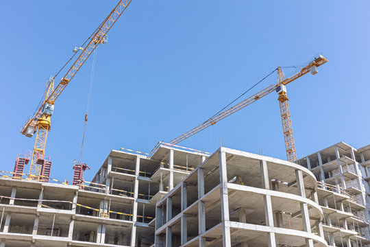 building tower cranes near apartment building under construction against blue sky background