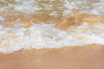 Fototapeta na wymiar White Splash Wave on the Surface of the Green Sea on the Golden Sand Beach and Blue Sky