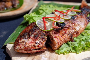 Fried fish with fresh green salad and lemon of Bali, Indonesia, closeup. Delicious roasted sea fish with lemon on wooden plate in restaurant