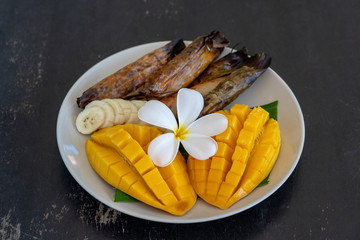 Thai style dessert, yellow mango with banana sticky rice in palm leaves. Yellow mango and sticky rice is popular traditional food of Thailand. Closeup