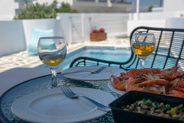 Two glasses of white wine and shrimps on the table by the pool.