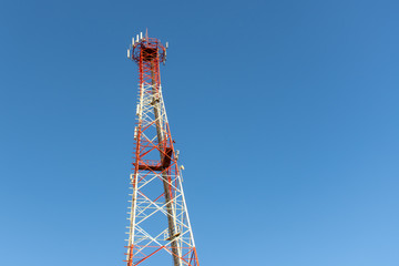 A red and white mobile or cell phone telecommunications tower on a blue sky background looking up.