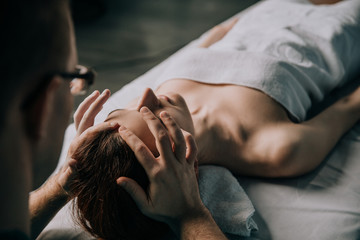 male masseur doing rejuvenating and relaxing face massage to young woman.