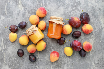 Peaches, plums and two jars with jam on gray stone background.