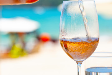 Pouring white wine in glasses at amazing sunset by the sea in beach cafe