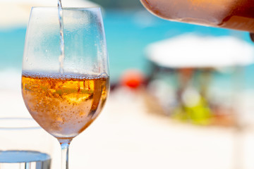 Pouring white wine in glasses at amazing sunset by the sea in beach cafe