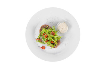 Steak beef with arugula, dried tomatoes and tartar, sour cream, mayonnaise, white sauce on a plate isolated white background, view from above
