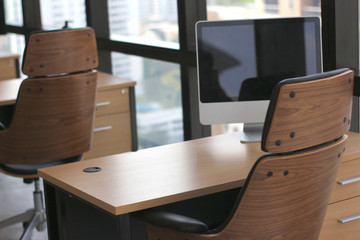 selective focus at wooden table desk in office business room with big computer monitor and windows background