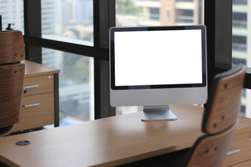 selective focus at wooden table desk in office business room with big computer monitor and windows background