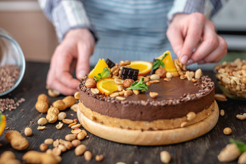 Confectioner decorates chocolate cake with orange and mint leaves with nuts. Concept healthy raw desserts for vegan food