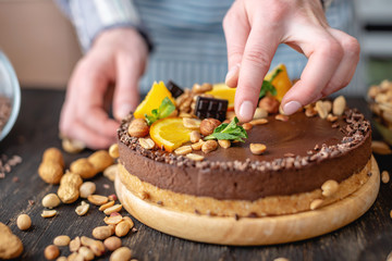 Obraz na płótnie Canvas Confectioner decorates chocolate cake with orange and mint leaves with nuts. Concept healthy raw desserts for vegan food