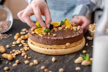 Confectioner decorates chocolate cake with orange and mint leaves with nuts. Concept healthy raw desserts for vegan food