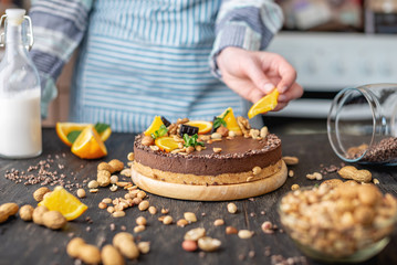 Confectioner decorates chocolate cake with orange and mint leaves with peanuts. Healthy raw desserts for vegan food