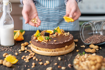 Confectioner decorates chocolate cake with orange and mint leaves with nuts. Concept healthy raw desserts for vegan food