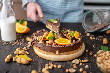 Pastry chef in hand holding a piece of chocolate cake with orange, mint and nuts. Healthy raw desserts for vegan food