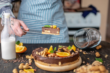 Pastry chef in hand holding a piece of chocolate cake with orange and peanuts. Healthy raw desserts for vegan food