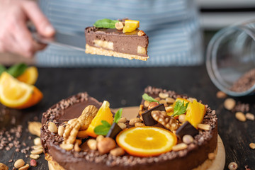 Pastry chef in hand holding a piece of chocolate cake with orange and peanuts. Healthy raw desserts for vegan food