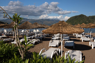 Beach in Marmaris, Turkey. Umbrellas of straw and white chaise lounges, bright blue sky and sea. Travel and vacation concept