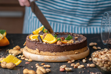 Confectioner decorates chocolate cake with orange and mint leaves with nuts. Concept healthy raw desserts for vegan food
