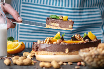 Pastry chef in hand holding a piece of chocolate cake with orange and peanuts. Healthy raw desserts for vegan food