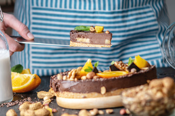 Pastry chef in hand holding a piece of chocolate cake with orange and peanuts. Healthy raw desserts for vegan food