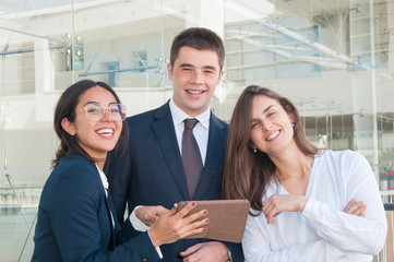 Three good looking colleagues standing  in office corridor, looking at camera, smiling. Work, communication concept