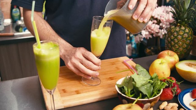 Man pouring mix of vegan fresh fruit smoothie with a selection of fruits on table