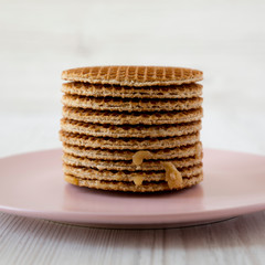 Stack of sweet Dutch stroopwafels with honey-caramel filling on a pink plate, side view. Close-up.