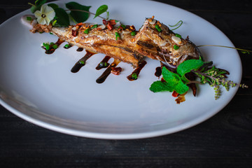 Fried Saba fish with Sauce on white plate and decoration by flower, vegetable and sauce plated on the wood table.