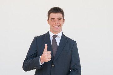 Cheerful sales agent recommending product or service. Young man in office jacket and tie showing thumb up and smiling at camera. Like gesture concept
