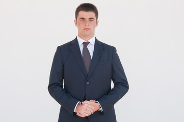 Serious office worker with clasped hands standing for camera. Portrait of young man in formal jacket and tie. Business portrait concept