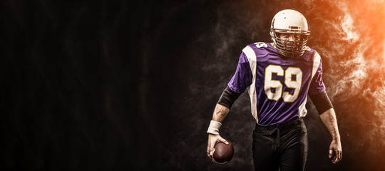 American football player holding ball in his hands in smoke. Black background, copy space. The concept of American football, motivation, copy space