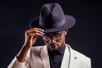 young handsome afro american melancholy boy in a white jacket and glasses on a black background in...
