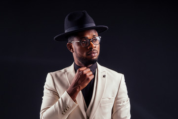 young handsome afro american melancholy boy in a white jacket and glasses on a black background in the studio.mystery and grief