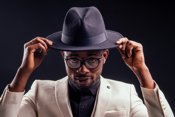 young handsome afro american melancholy boy in a white jacket and glasses on a black background in...