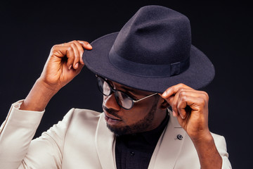 young handsome afro american melancholy boy in a white jacket and glasses on a black background in the studio.mystery and grief