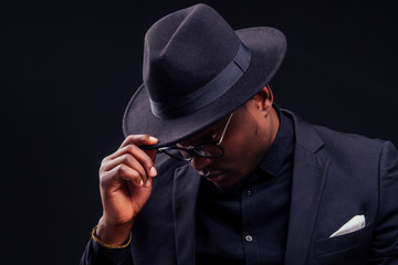 young handsome afro american melancholy boy in a jacket and glasses on a black background in the studio.mystery and grief hide