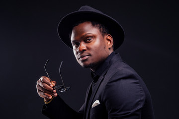 young handsome afro american melancholy boy in a jacket and glasses on a black background in the studio.mystery and grief hide