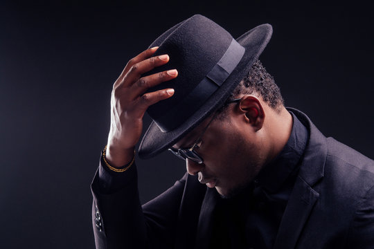 young handsome afro american melancholy boy in a jacket and glasses on a black background in the studio.mystery and grief hide