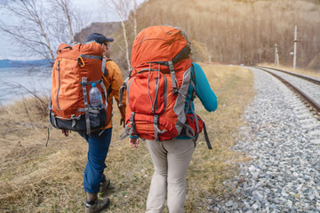 Tourists Hiking with orange backpacks are on the old railway at the foot of the mountain. Travel to...