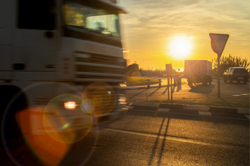Two trucks drive in a roundabout and in the background the sun rises over the Mediterranean Sea.
