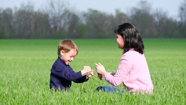 Happy child and mom play on the green grass in the park, hug and kiss