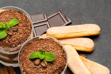 Classic tiramisu dessert in a glass and savoiardi cookies on dark concrete background