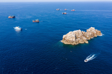 Industrial overfishing - Aerial view of a SCUBA diving boat and a fleet of large fishin trawlers near a small rocky island (Black Rock, Mergui, Myanmar)